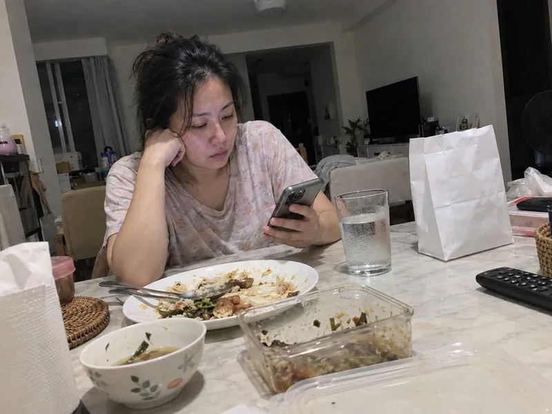 女士晚上坐在餐桌前看手机，晚餐没吃几口，旁边放着药房纸袋