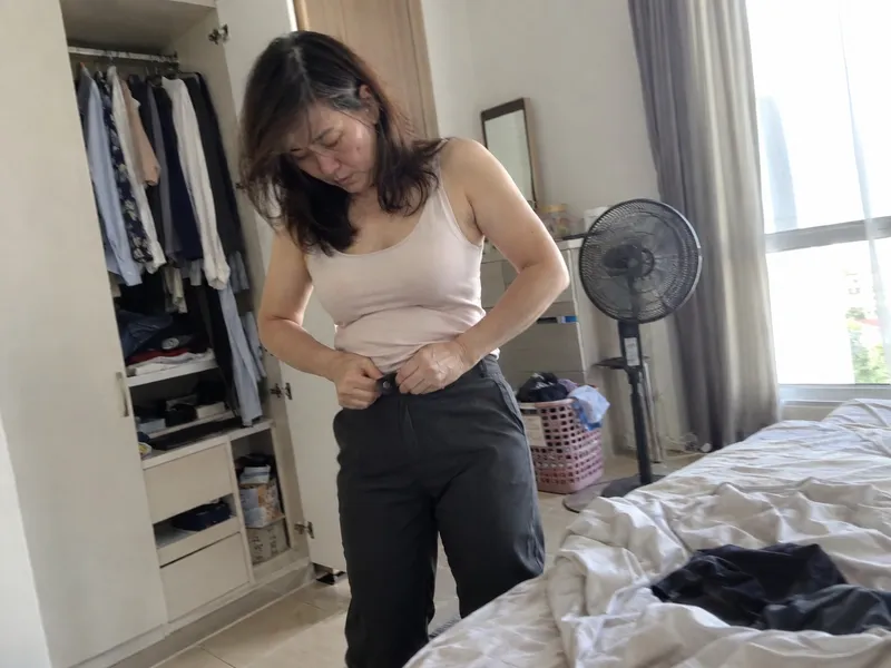 40 多岁的女士早上在房间换衣服，扣不上变紧的裤头